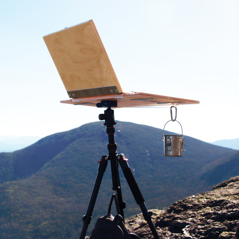 u.go Plein Air Anywhere Pochade Box, 11" x 14.5" model, with u.go Cinch and u.go Carabiner on tripod while landscape plain air painting