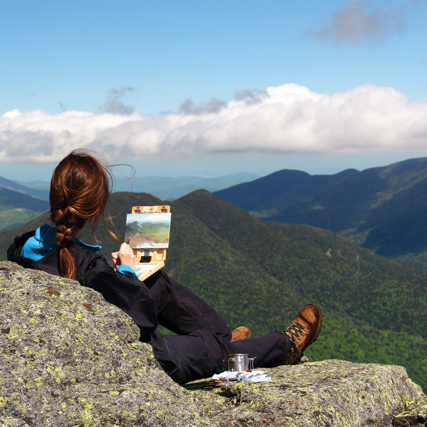 u.go Plein Air Anywhere Pochade Box, 6" x 8" model, placed on knee while plein air landscape painting