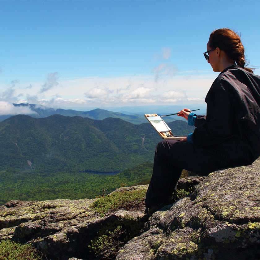 u.go Plein Air Anywhere Pochade Box, 6" x 8" model, placed on lap while plein air landscape painting